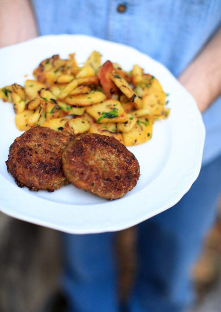 Faschierte Laibchen mit Karotten und Zucchini auf einem Teller mit Bratkartoffeln angerichtet